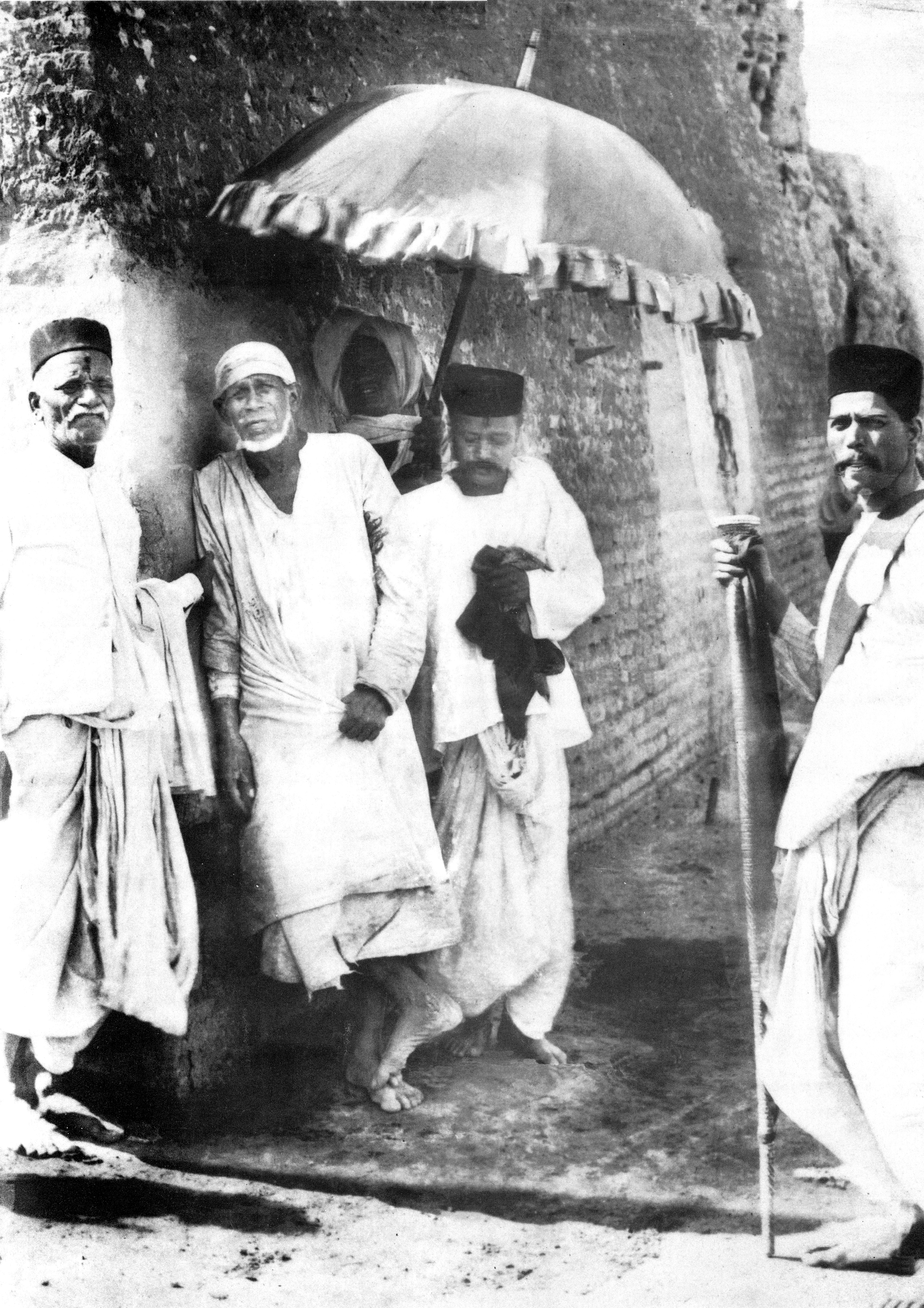 Sai Baba Leaning against the wall of his Mosque in which he stayed and prayed